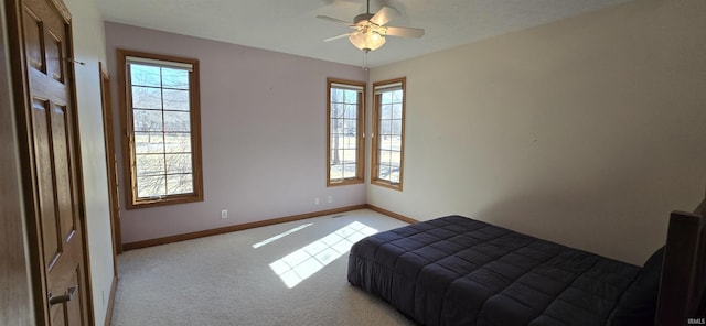 bedroom with a ceiling fan, light colored carpet, multiple windows, and baseboards