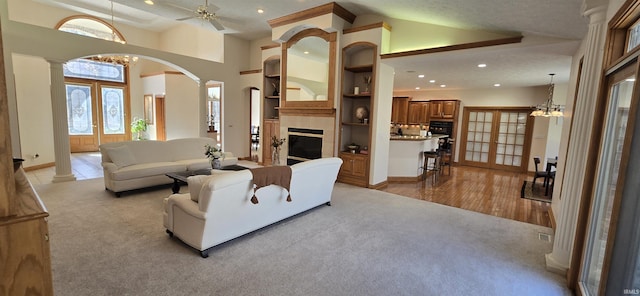 living room with light carpet, decorative columns, arched walkways, a tile fireplace, and recessed lighting