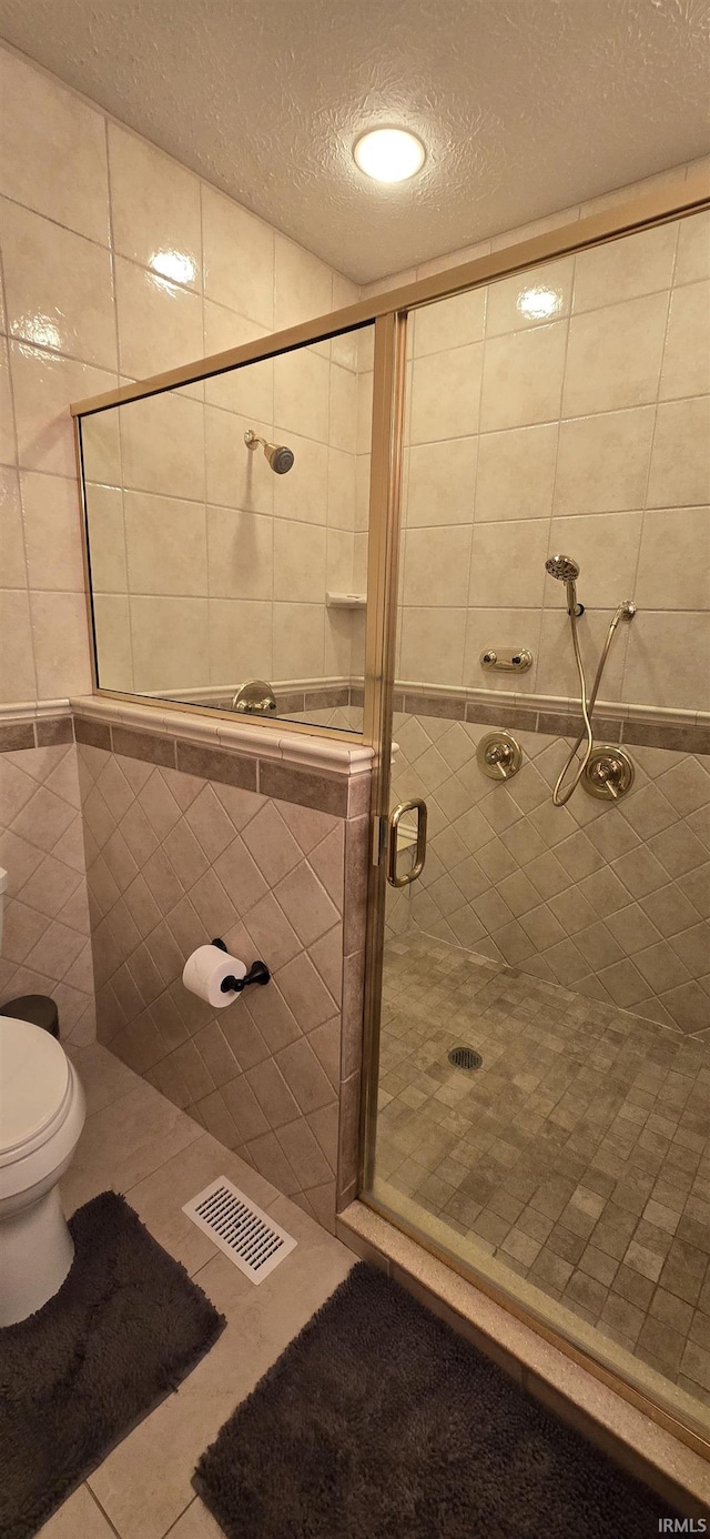 full bath featuring a textured ceiling, tile patterned flooring, visible vents, tile walls, and a shower stall