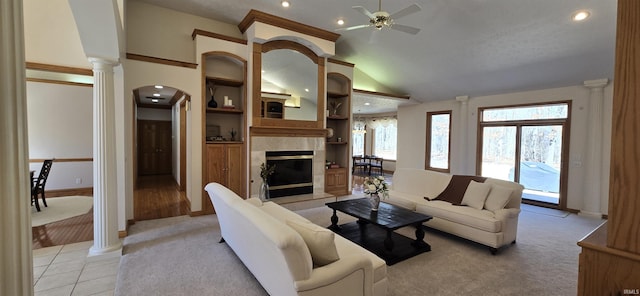 living area featuring decorative columns, arched walkways, a ceiling fan, a tiled fireplace, and vaulted ceiling