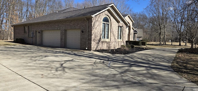 view of property exterior featuring an attached garage, concrete driveway, and brick siding