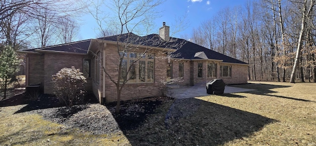 view of side of home featuring a yard, a patio, brick siding, and a chimney