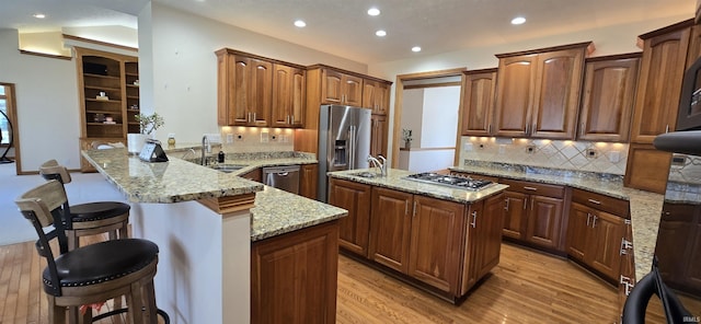 kitchen featuring appliances with stainless steel finishes, a center island, a peninsula, light stone countertops, and a kitchen bar