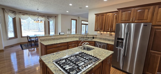 kitchen with appliances with stainless steel finishes, a sink, light stone countertops, and pendant lighting