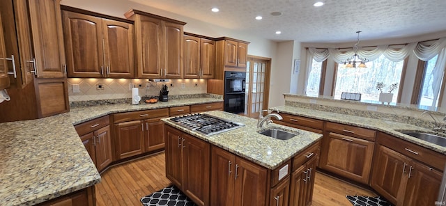 kitchen with light stone countertops, a kitchen island with sink, stainless steel gas stovetop, pendant lighting, and a sink