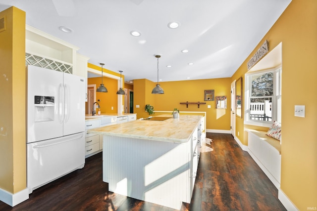 kitchen with hanging light fixtures, white refrigerator with ice dispenser, white cabinets, and an island with sink