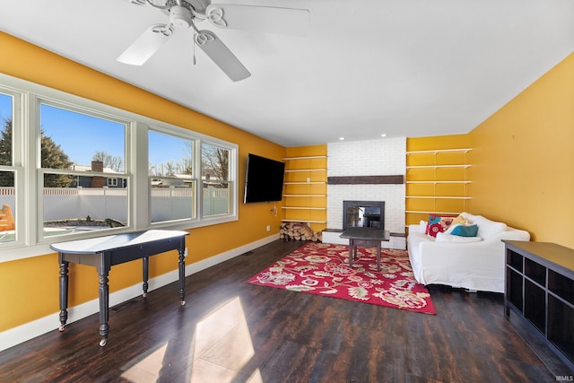 living room featuring dark wood-style floors, a brick fireplace, ceiling fan, and baseboards