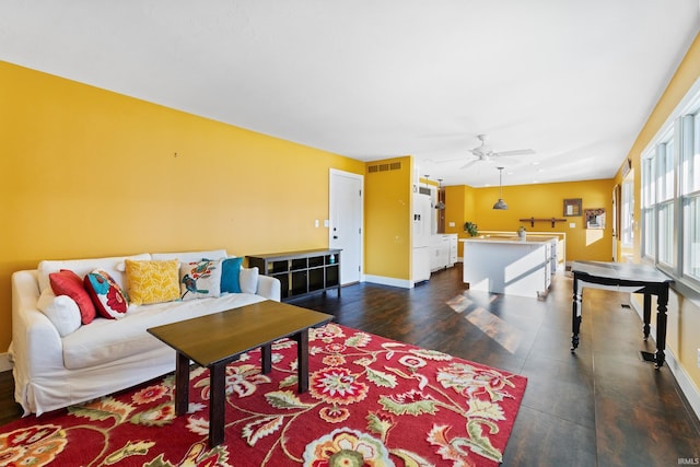 living room with dark wood-style flooring, visible vents, ceiling fan, and baseboards