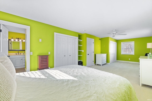 bedroom with connected bathroom, light carpet, a sink, baseboards, and two closets