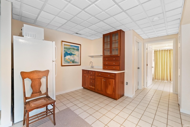 kitchen featuring light countertops, freestanding refrigerator, brown cabinetry, and glass insert cabinets