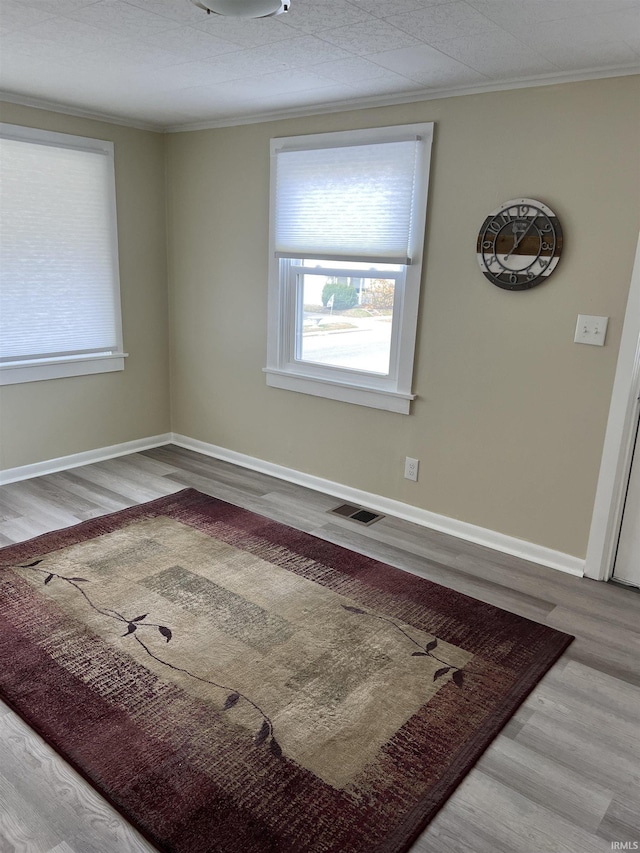 empty room with ornamental molding, visible vents, baseboards, and wood finished floors