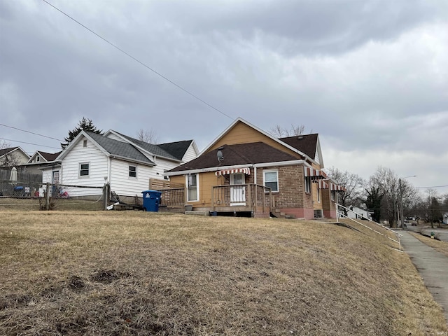 view of front of house featuring brick siding, a wooden deck, and a front yard