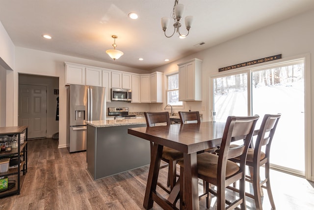 kitchen featuring dark wood-style flooring, decorative light fixtures, stainless steel appliances, white cabinetry, and light stone countertops