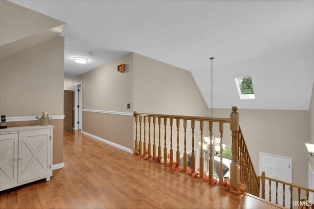 hallway featuring lofted ceiling with skylight, an upstairs landing, light wood-style flooring, and baseboards