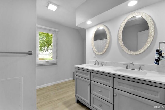 full bathroom with double vanity, baseboards, a sink, and wood finished floors