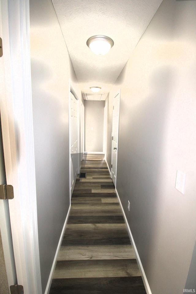 hall with a textured ceiling, baseboards, and dark wood-type flooring