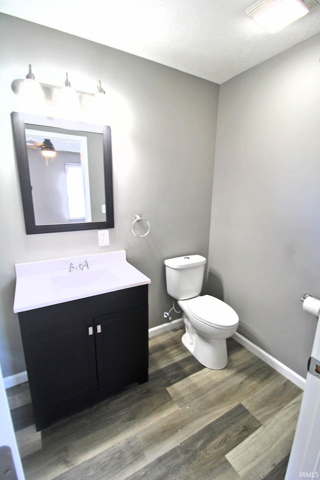 half bath featuring a textured ceiling, toilet, wood finished floors, vanity, and baseboards