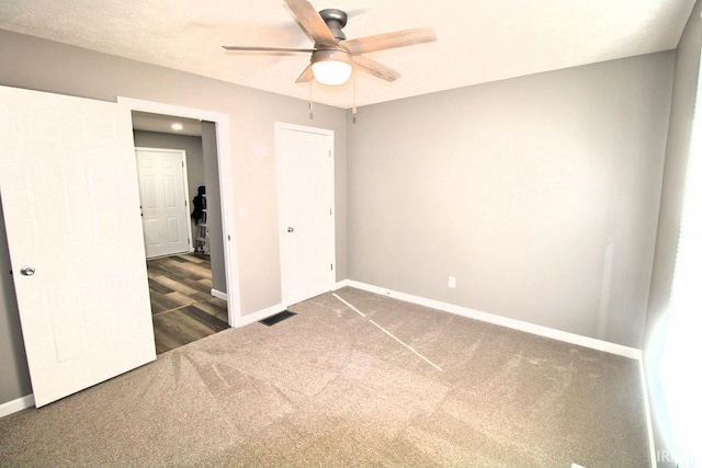 empty room with baseboards, dark carpet, and a ceiling fan