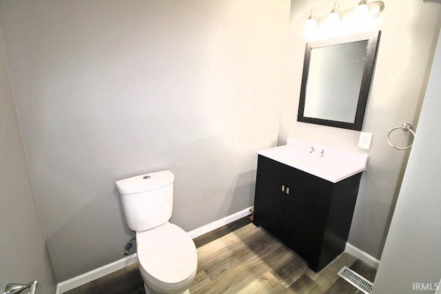 half bathroom with vanity, wood finished floors, visible vents, and baseboards