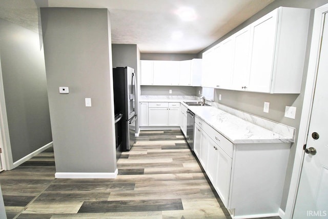 kitchen with light countertops, appliances with stainless steel finishes, white cabinets, a sink, and wood finished floors