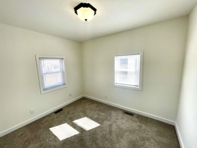 unfurnished room with dark colored carpet, visible vents, and baseboards