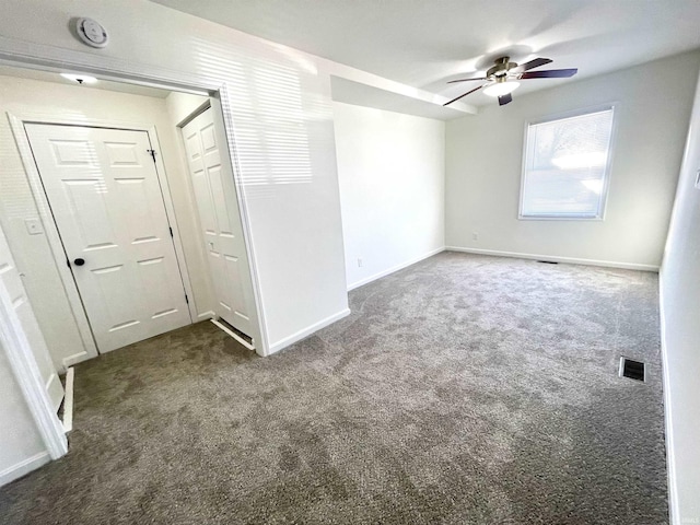 empty room featuring a ceiling fan, visible vents, dark carpet, and baseboards