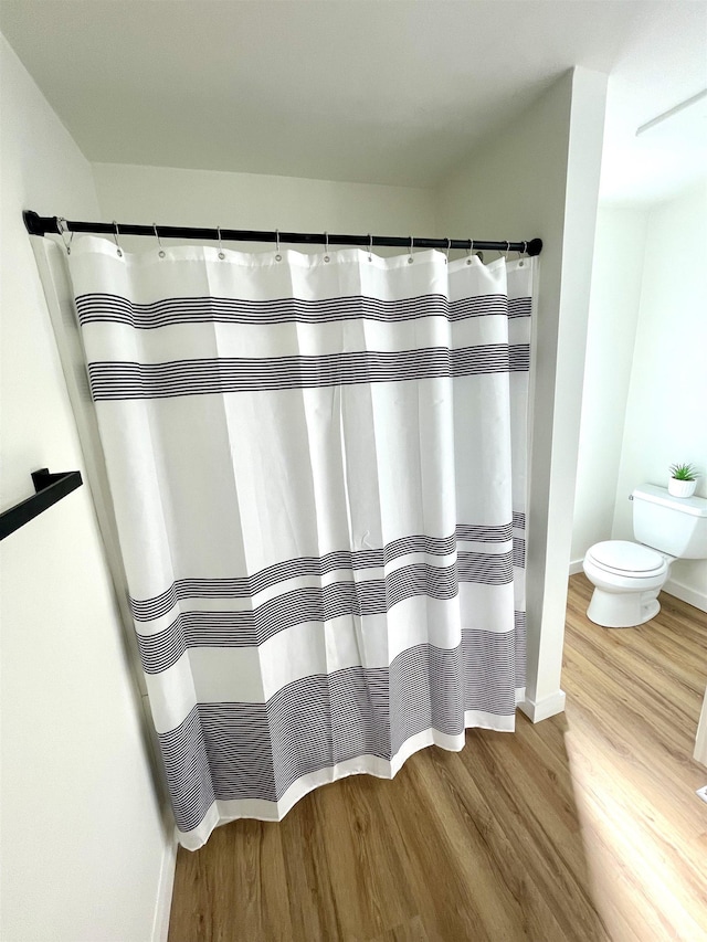 bathroom featuring curtained shower, wood finished floors, toilet, and baseboards