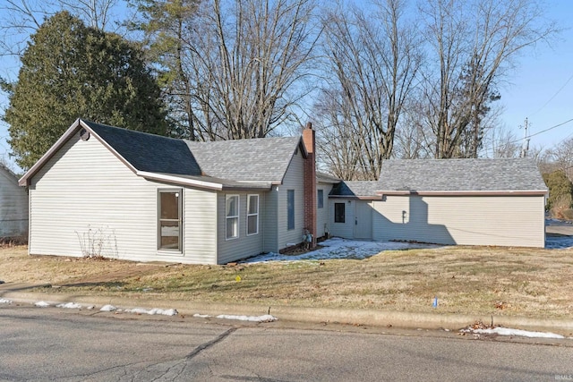 view of front of house with a shingled roof, a chimney, and a front yard