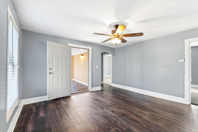 empty room featuring a ceiling fan, baseboards, arched walkways, and dark wood-type flooring