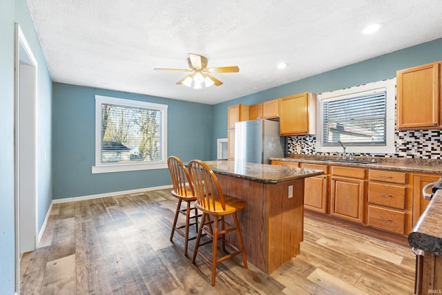 kitchen featuring tasteful backsplash, a breakfast bar area, freestanding refrigerator, a center island, and a sink