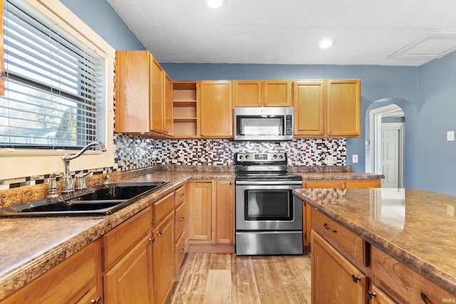 kitchen featuring arched walkways, backsplash, appliances with stainless steel finishes, light wood-style floors, and a sink