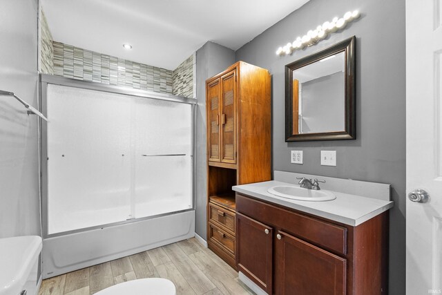 bathroom with toilet, bath / shower combo with glass door, wood finished floors, and vanity