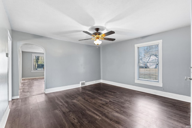 spare room featuring arched walkways, ceiling fan, visible vents, baseboards, and dark wood-style floors