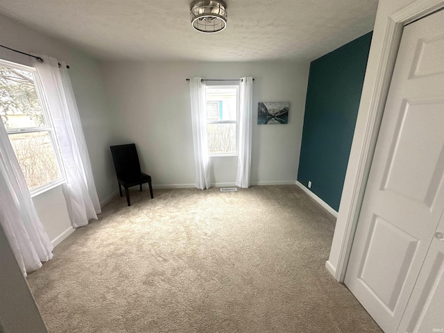 interior space featuring visible vents, baseboards, a textured ceiling, and light colored carpet