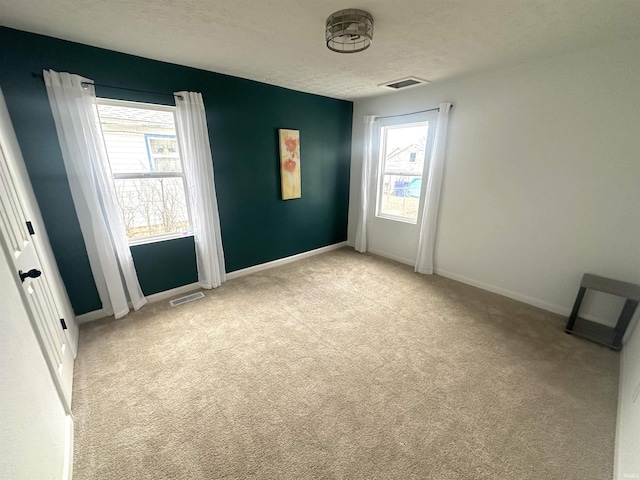 unfurnished room with a textured ceiling, baseboards, visible vents, and light colored carpet