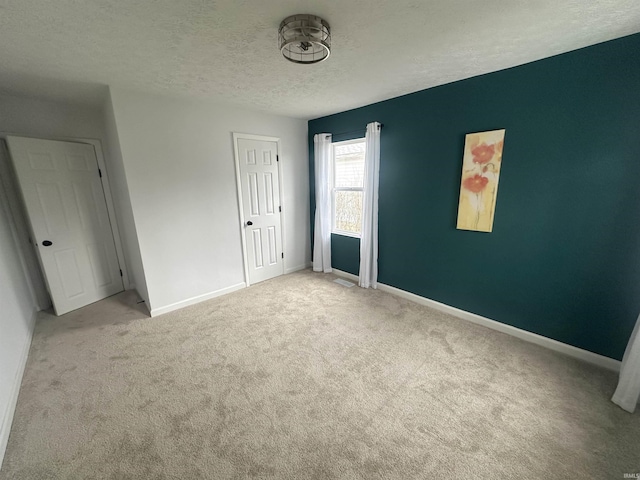 unfurnished bedroom featuring a textured ceiling, baseboards, and light colored carpet