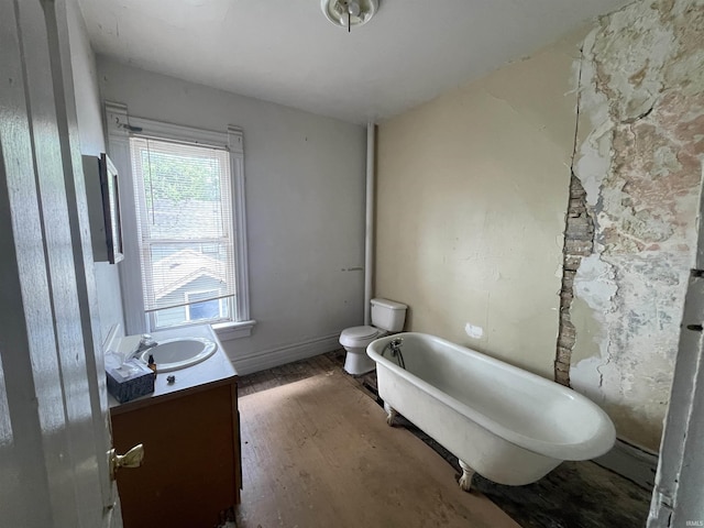 bathroom featuring toilet, vanity, wood finished floors, a freestanding tub, and baseboards