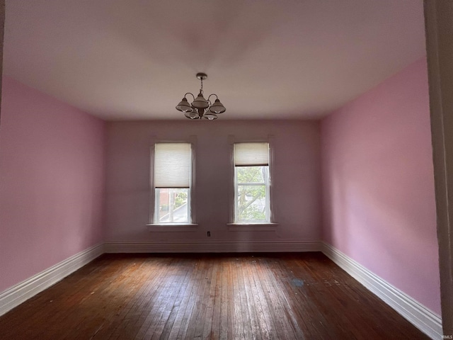 spare room featuring a chandelier, dark wood-style flooring, and baseboards