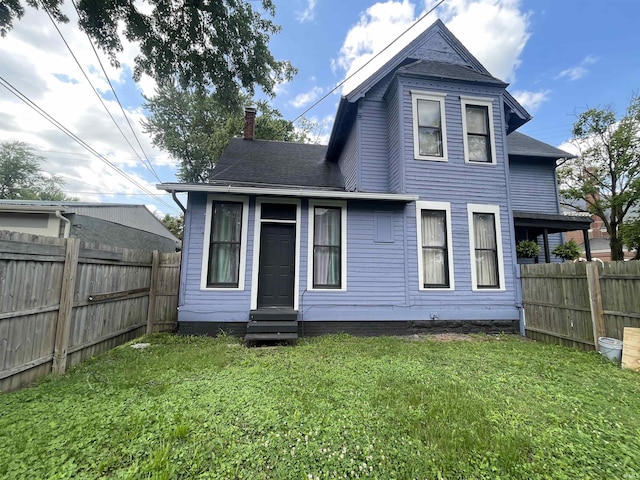 rear view of property featuring entry steps, a chimney, fence, and a lawn