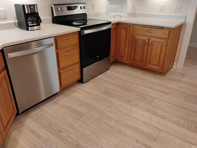 kitchen featuring brown cabinetry, light wood-style flooring, stainless steel appliances, and light countertops