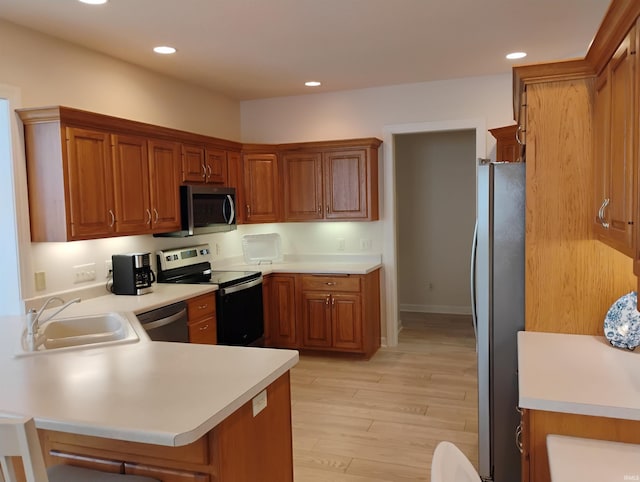 kitchen featuring light countertops, appliances with stainless steel finishes, brown cabinetry, a sink, and a peninsula