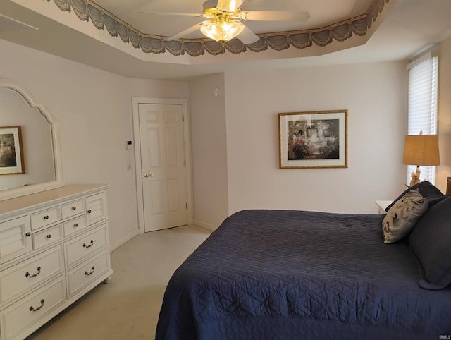 bedroom featuring light carpet, a tray ceiling, a ceiling fan, and baseboards