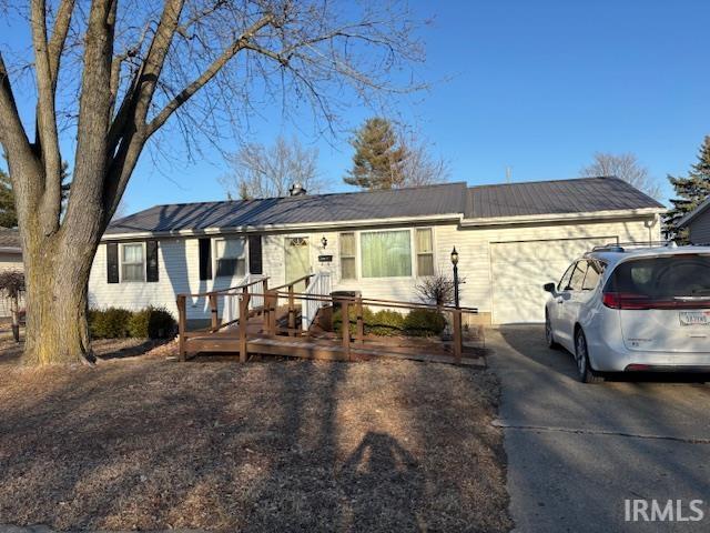 ranch-style home with a garage, metal roof, and driveway