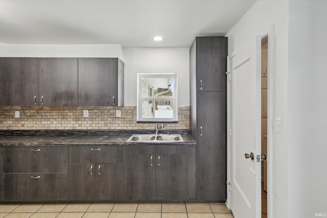 kitchen featuring tasteful backsplash, dark countertops, light tile patterned flooring, a sink, and dark brown cabinets