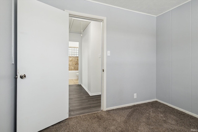 unfurnished room with attic access, dark colored carpet, crown molding, and baseboards