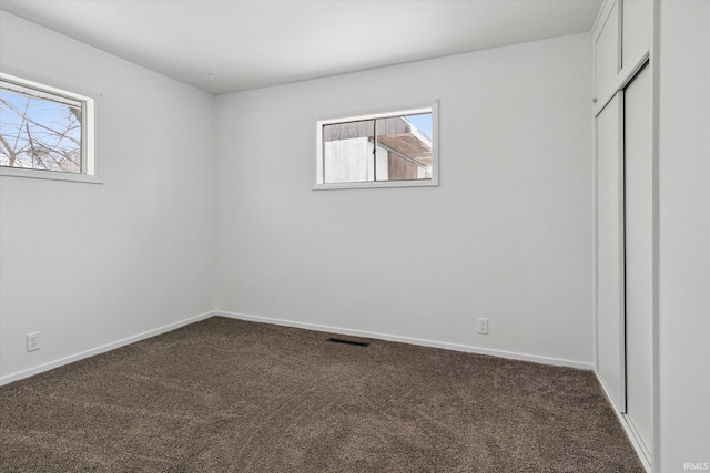 unfurnished bedroom with dark colored carpet, visible vents, and baseboards