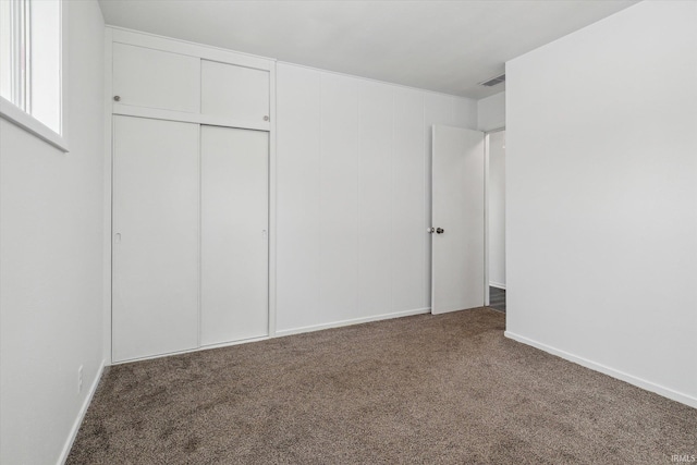 unfurnished bedroom featuring dark colored carpet, a closet, visible vents, and baseboards