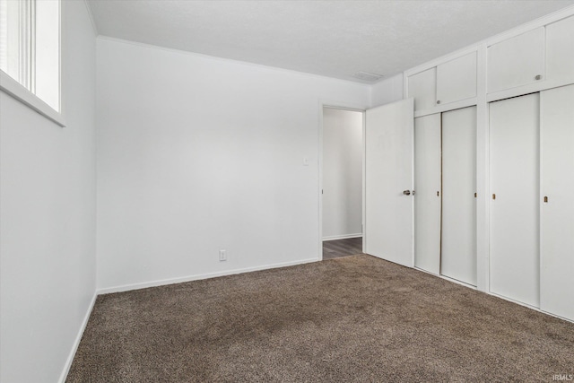 unfurnished bedroom featuring baseboards, dark carpet, and multiple closets