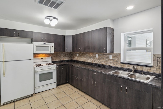 kitchen with light tile patterned floors, white appliances, a sink, dark brown cabinets, and dark countertops