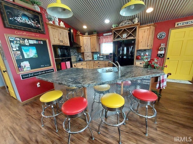 kitchen featuring dark wood-style floors, wall chimney range hood, dark countertops, and a sink